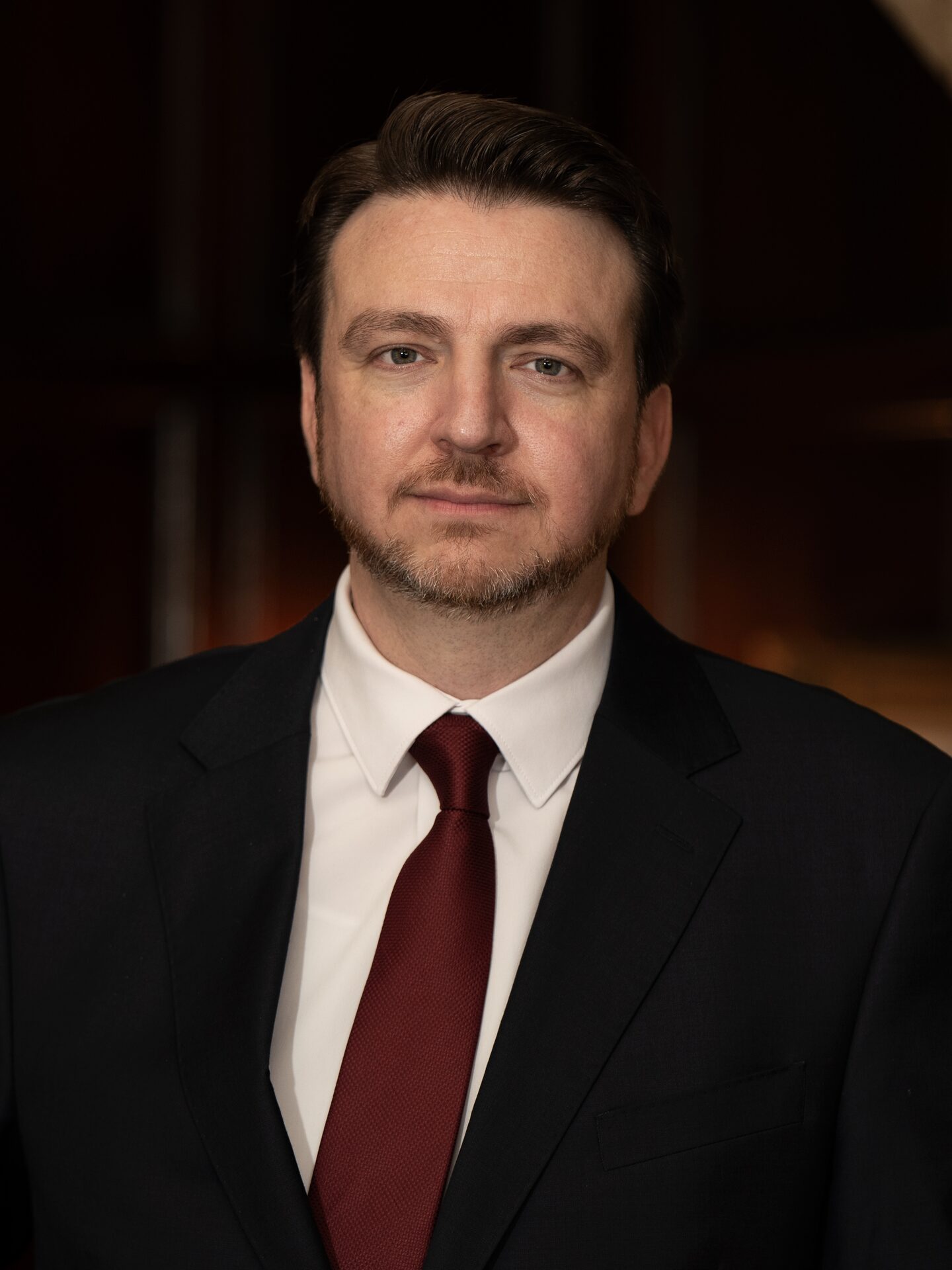 Philip Foust in a dark suit and red tie, photographed in a wood-paneled hallway.